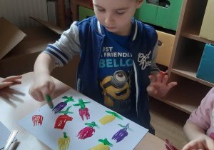 Mateusz palcem maluje łodyżki i liście tulipanów.
